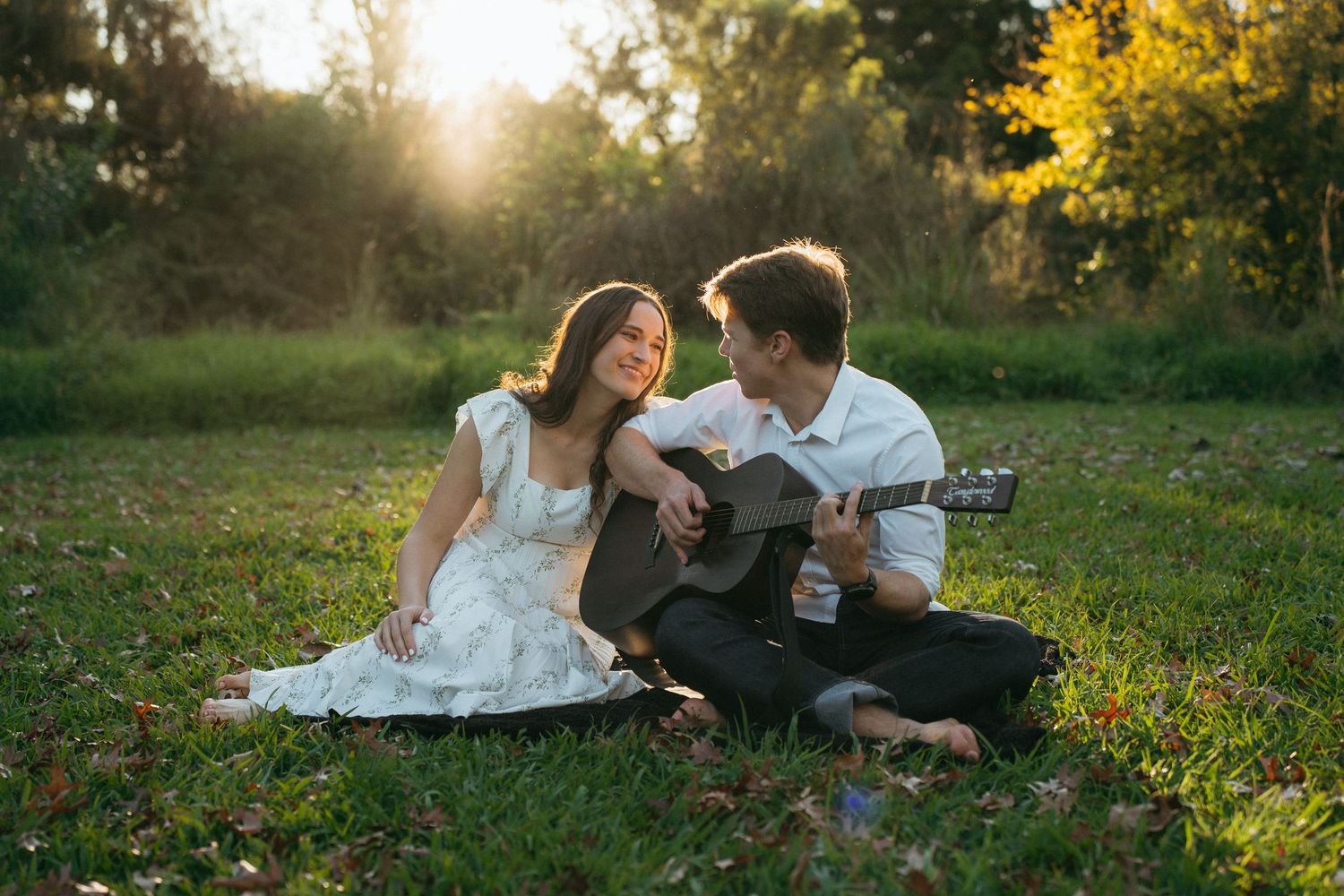 A couple shares a romantic moment in a sunlit meadow while playing acoustic guitar during golden hour.