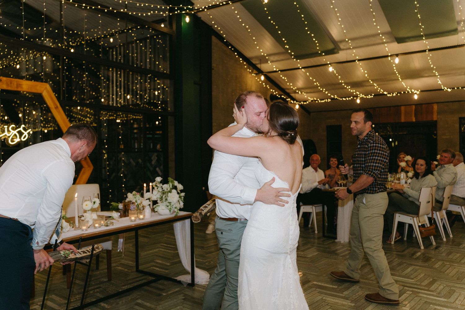 Wedding reception celebration with dancing and string lights in an indoor venue.