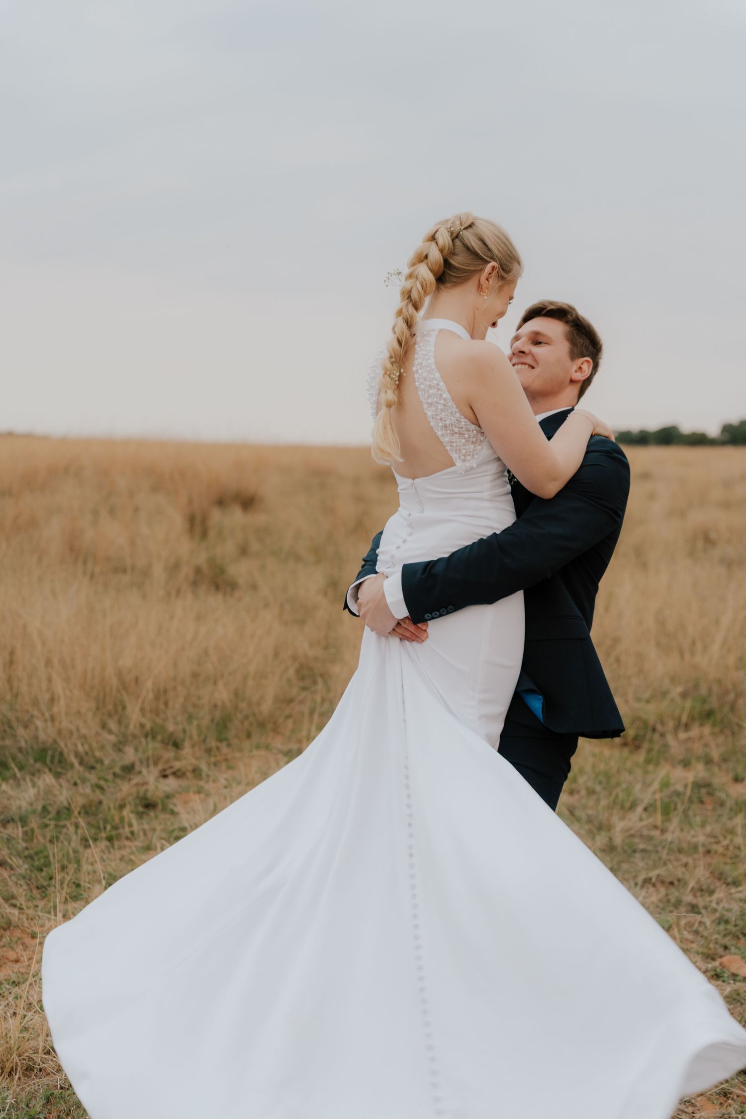 A couple in wedding attire dances and twirls in a golden wheat field during sunset.