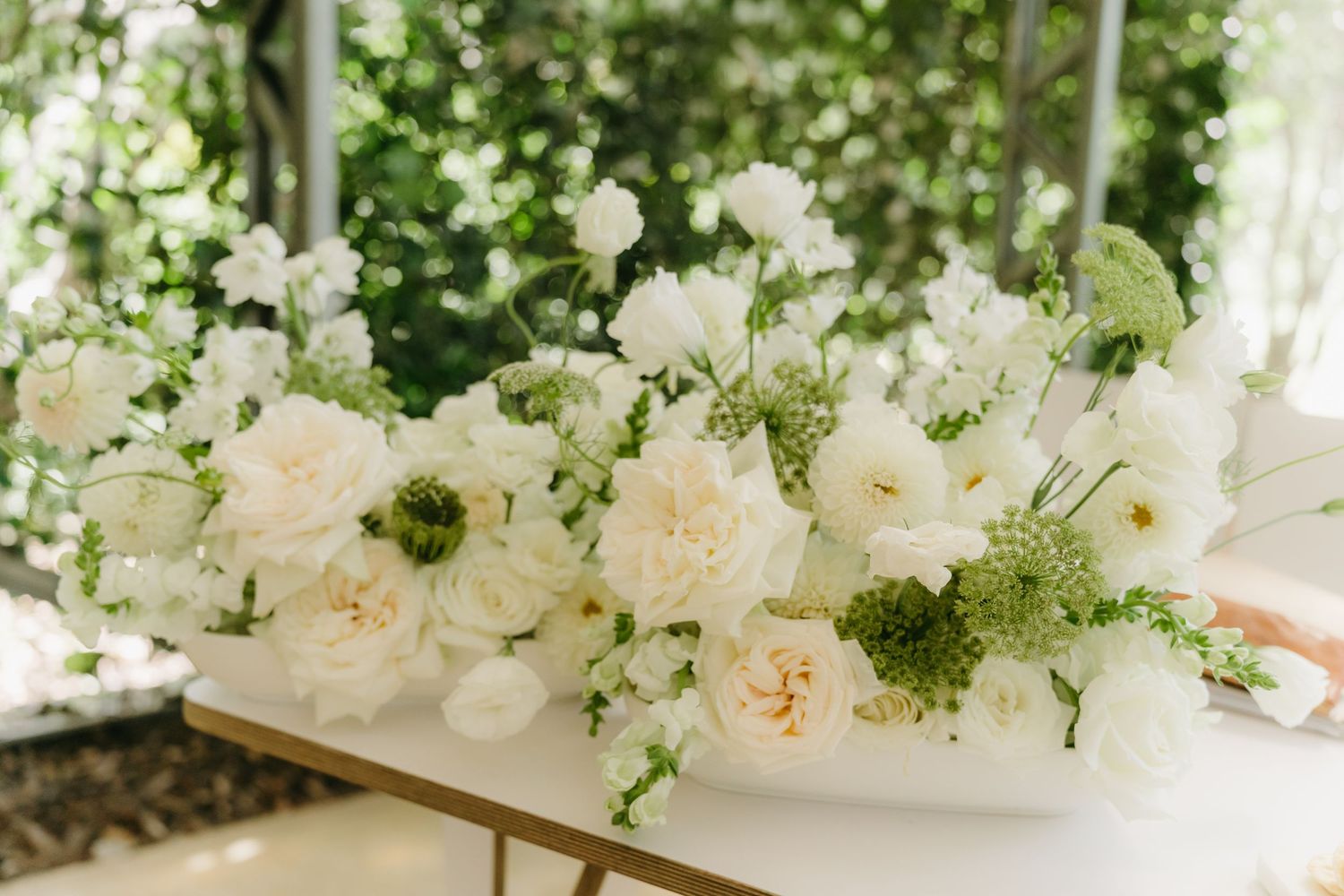 Elegant white and cream floral centerpiece arrangement with roses and delicate greenery on a light surface.