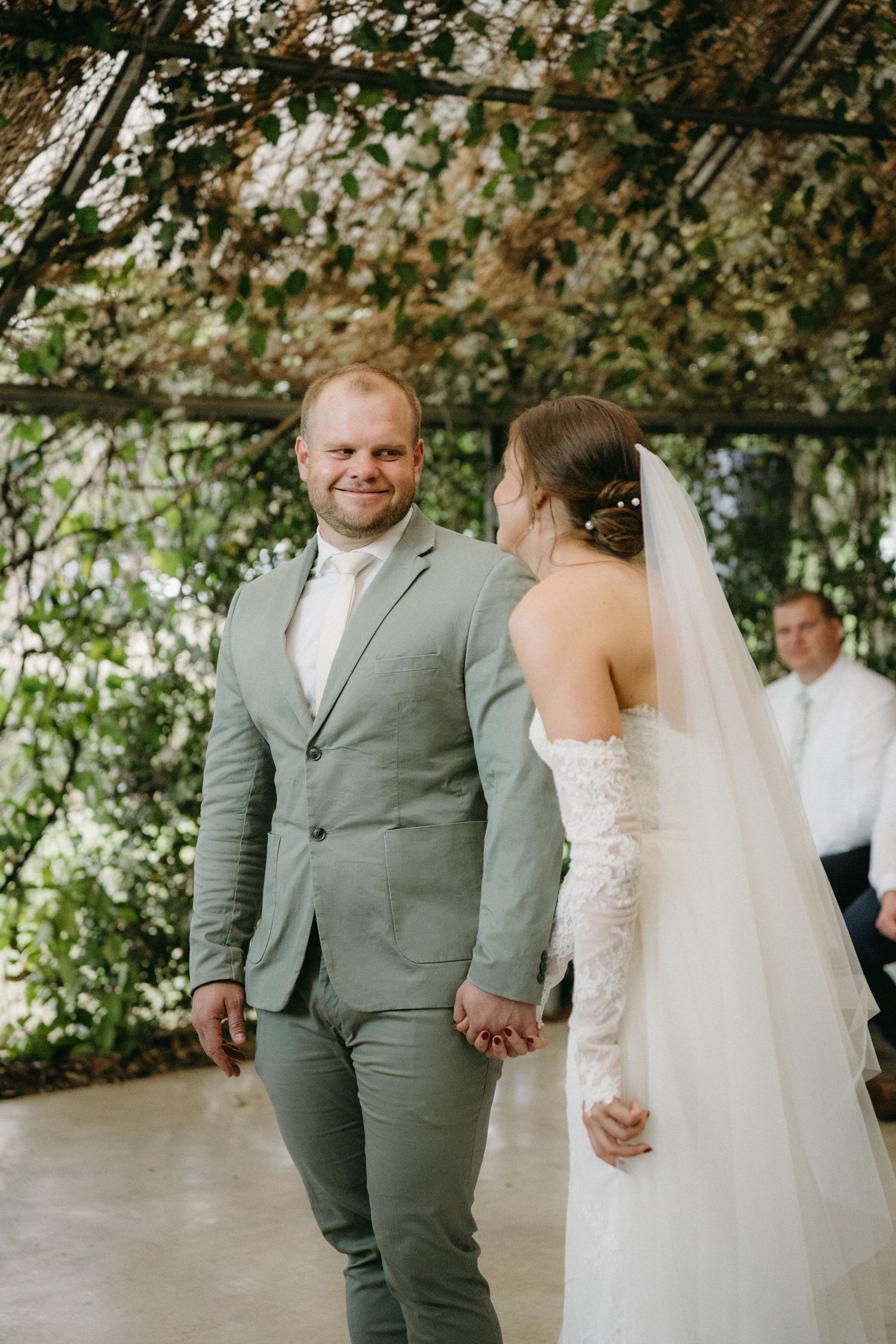 A bride and groom share a joyful moment under a leafy canopy during their outdoor wedding ceremony.