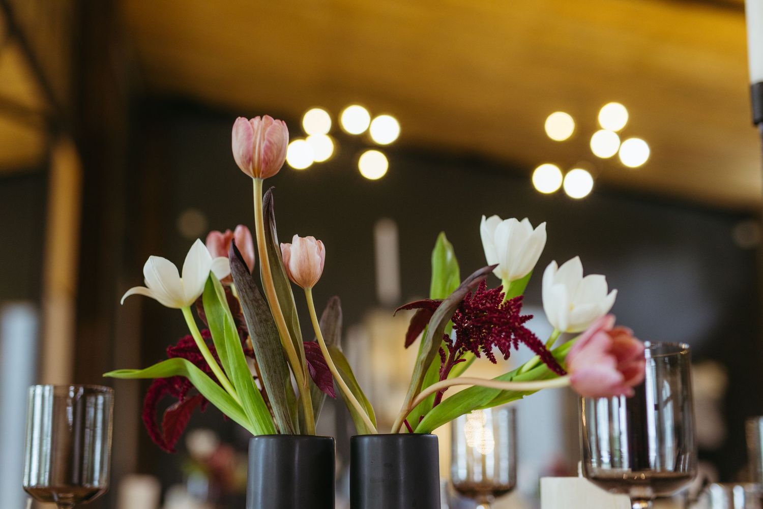 Elegant floral centerpiece with pink and white tulips in black vases under warm lighting.
