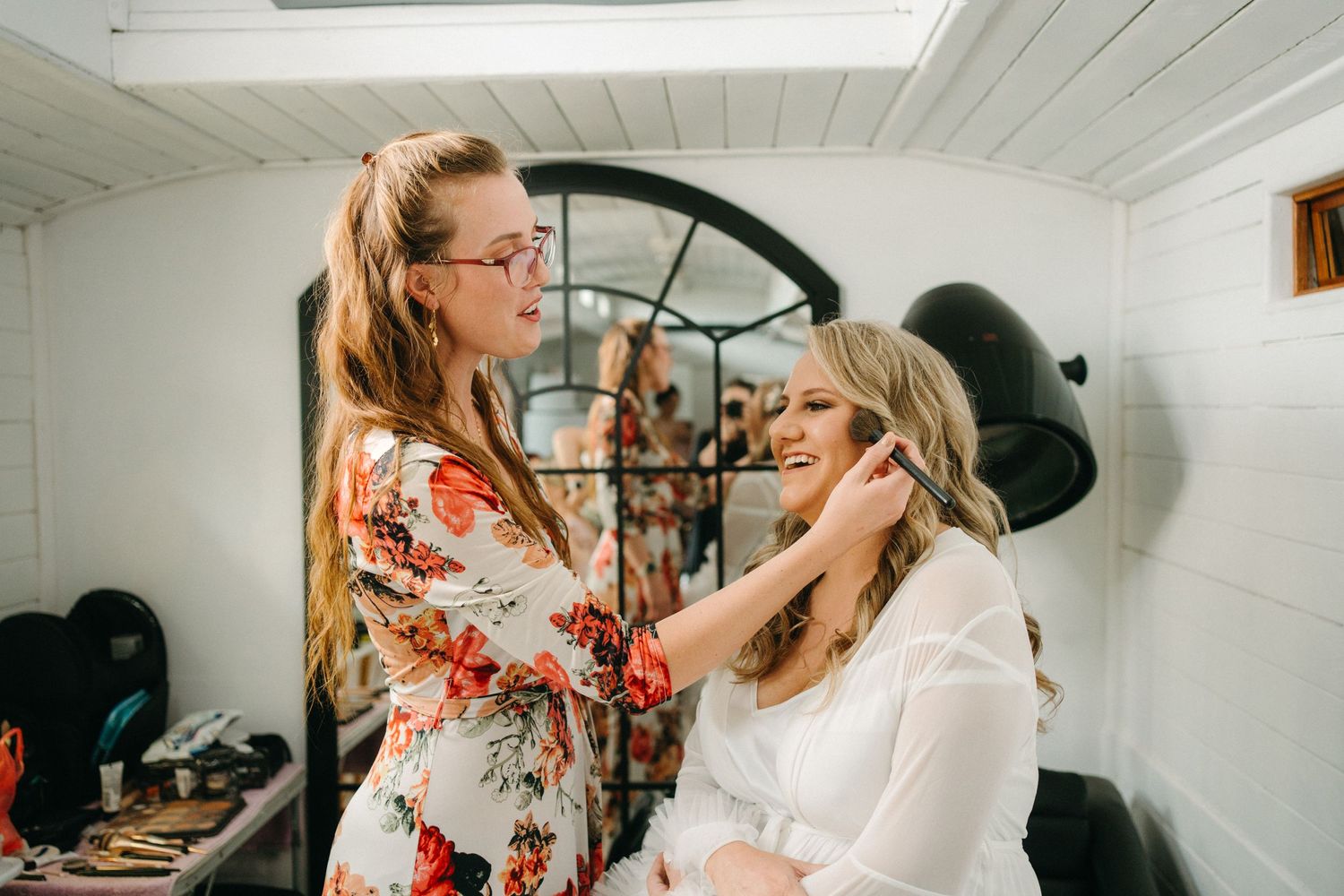 Wedding preparation scene with makeup application in bright white room with circular window.