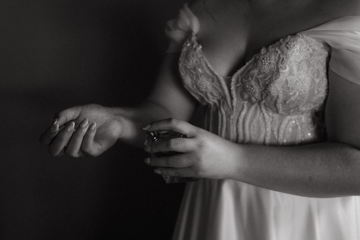 Close-up black and white detail of hands against a white lace dress with delicate details.