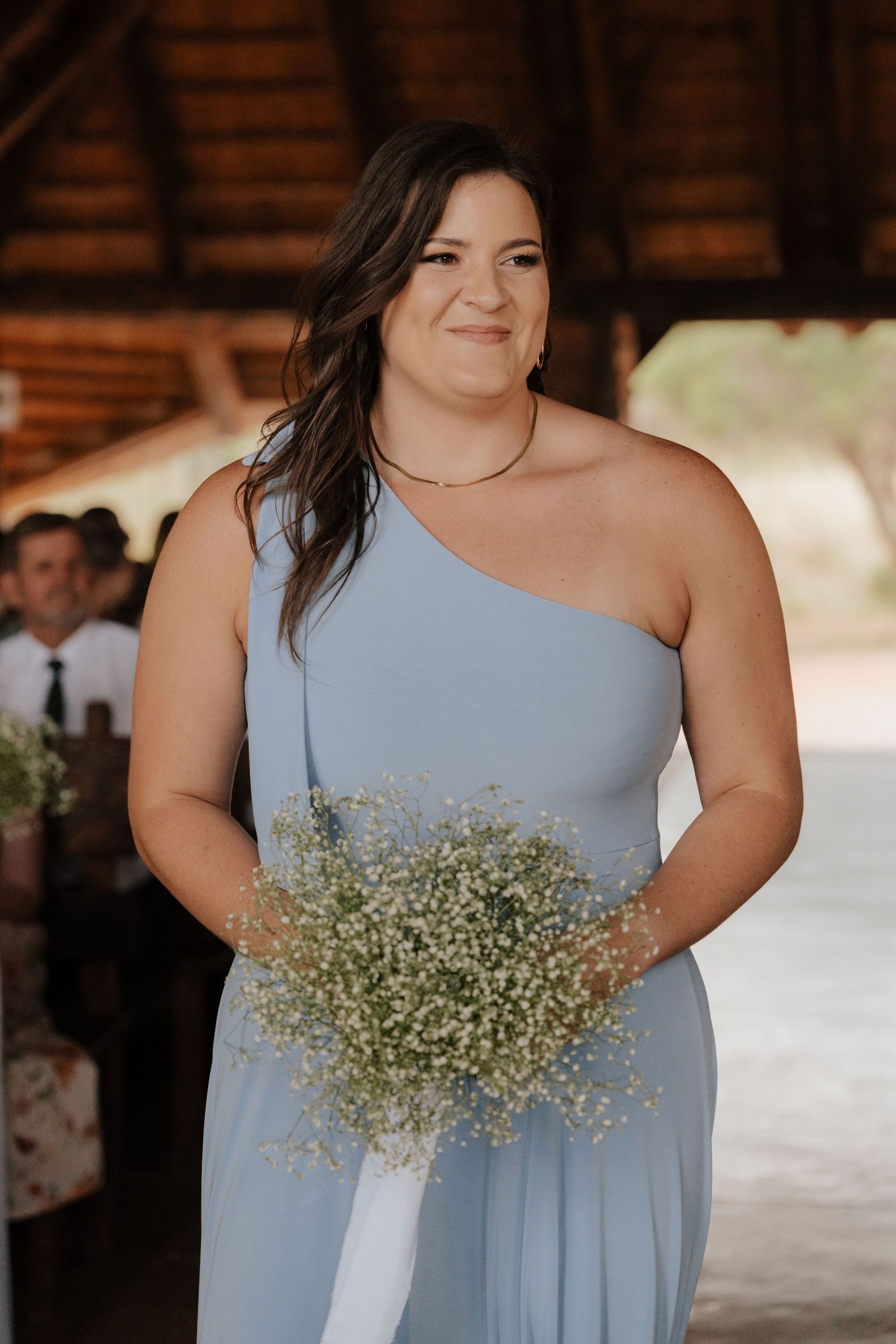 Bridesmaid in light blue dress holding delicate baby's breath bouquet.