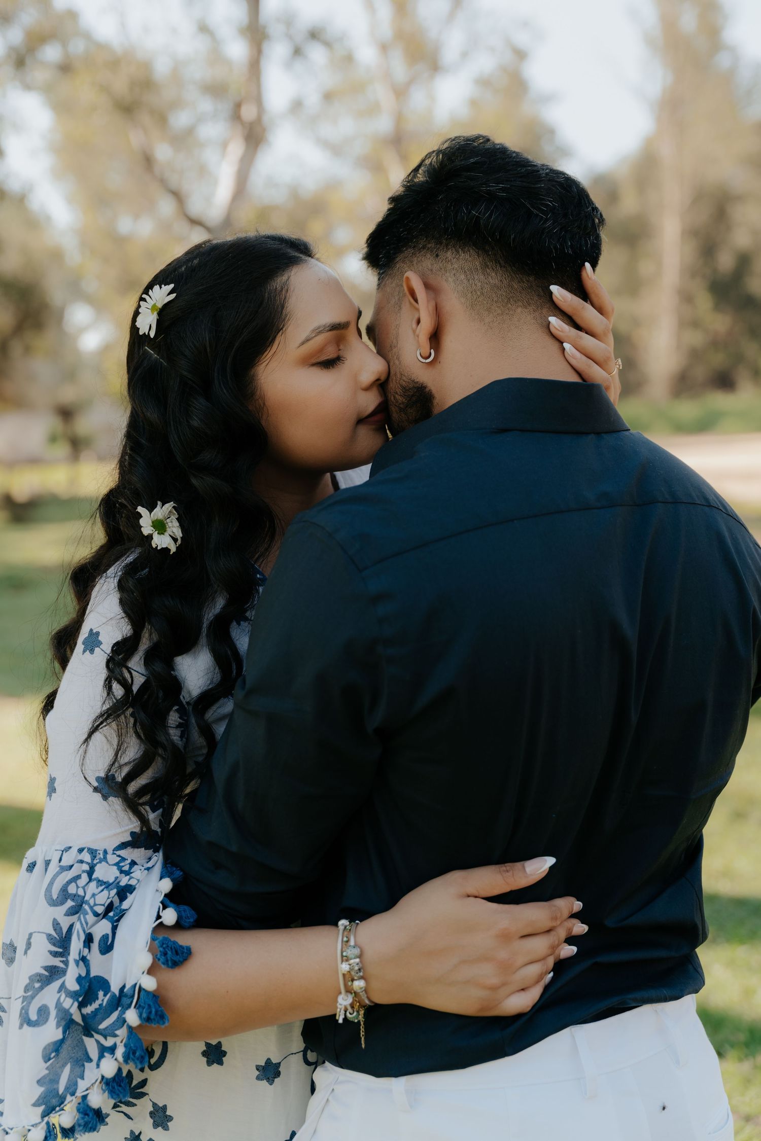 A romantic couple embraces and shares tender moments in a natural outdoor setting with trees in the background.
