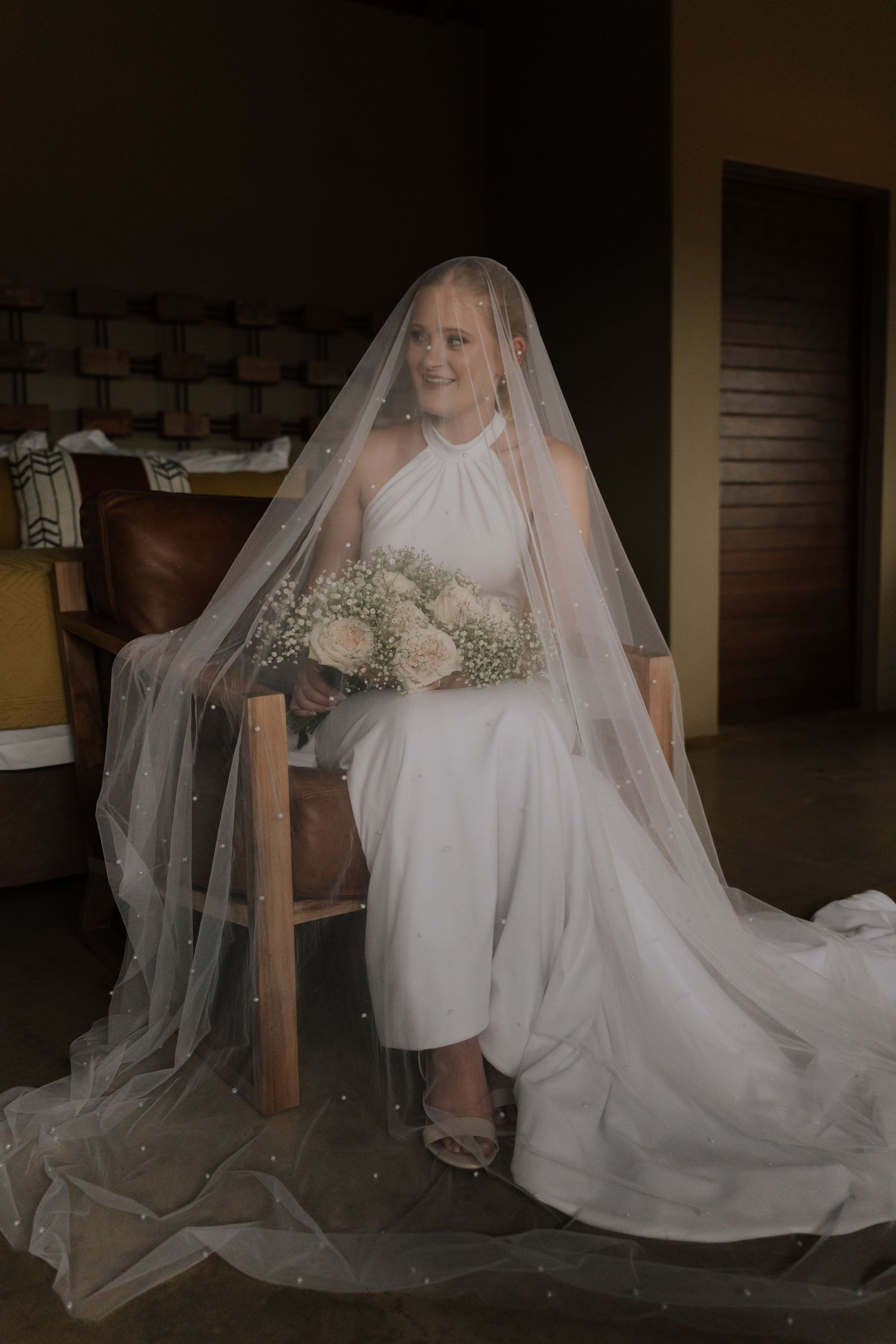 A bride in a flowing white gown and veil sits elegantly in preparation for her wedding day.