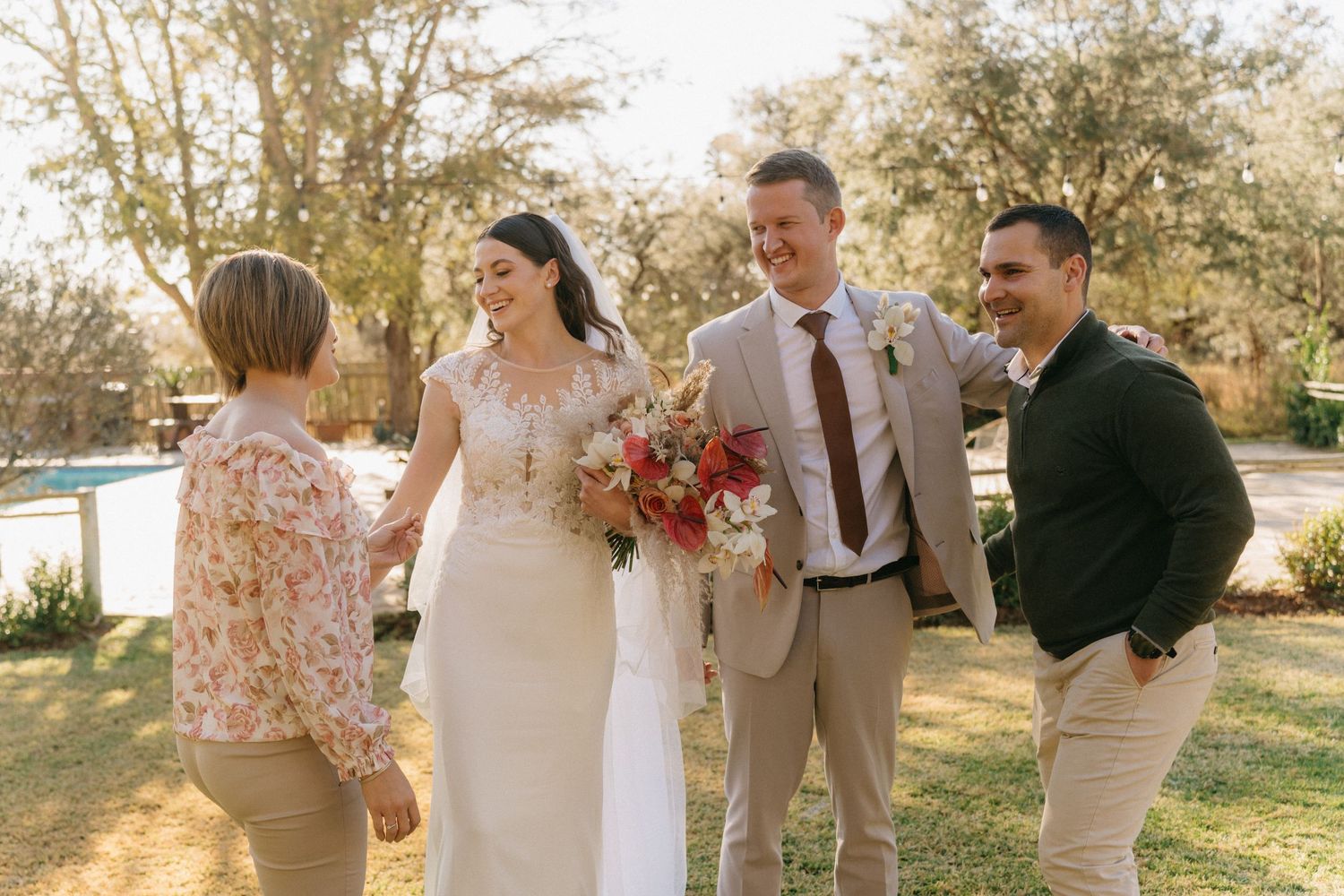 Wedding party poses outdoors in natural sunlight with tan and white attire.