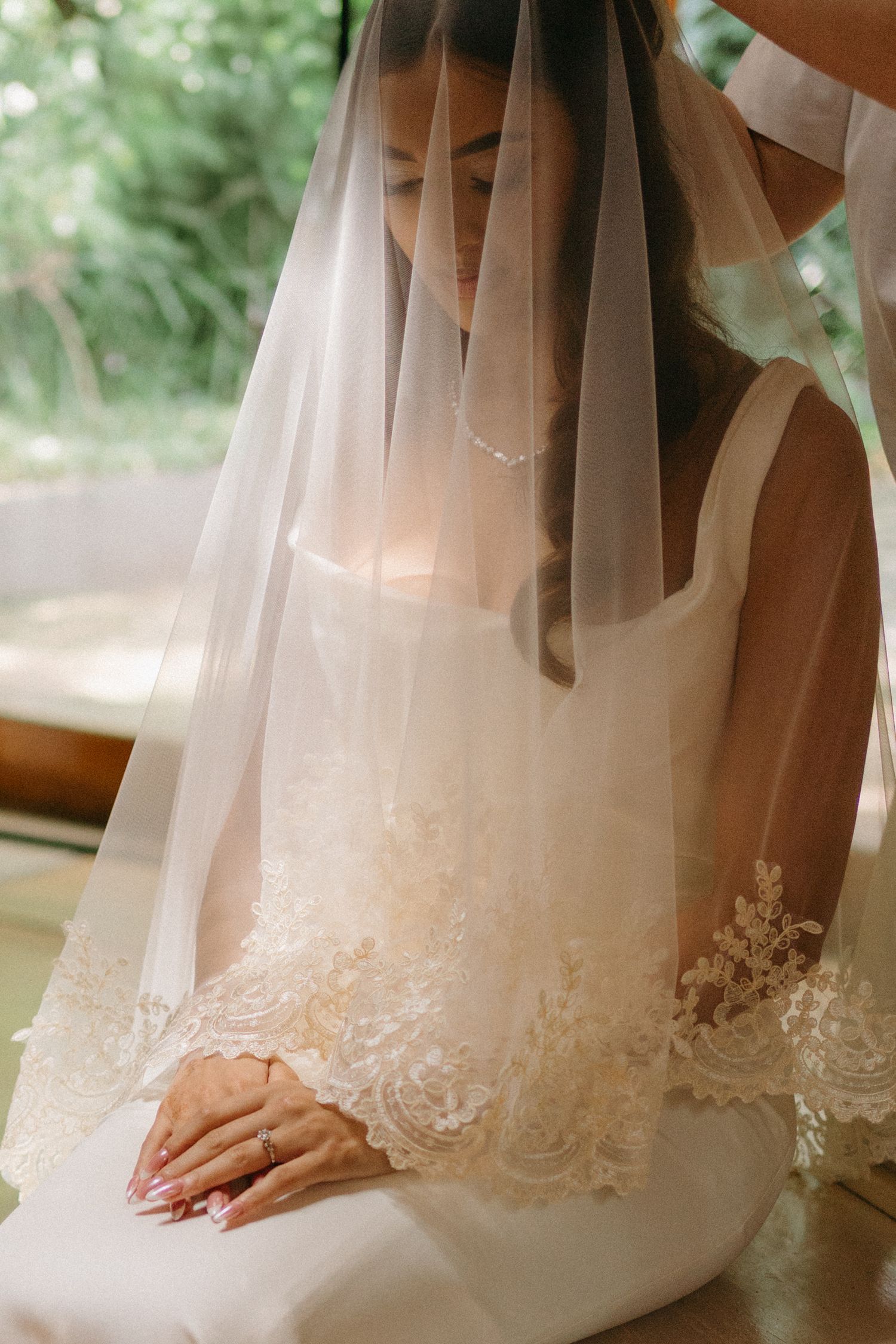 A delicate bridal moment showing lace veil details and clasped hands in soft natural light.