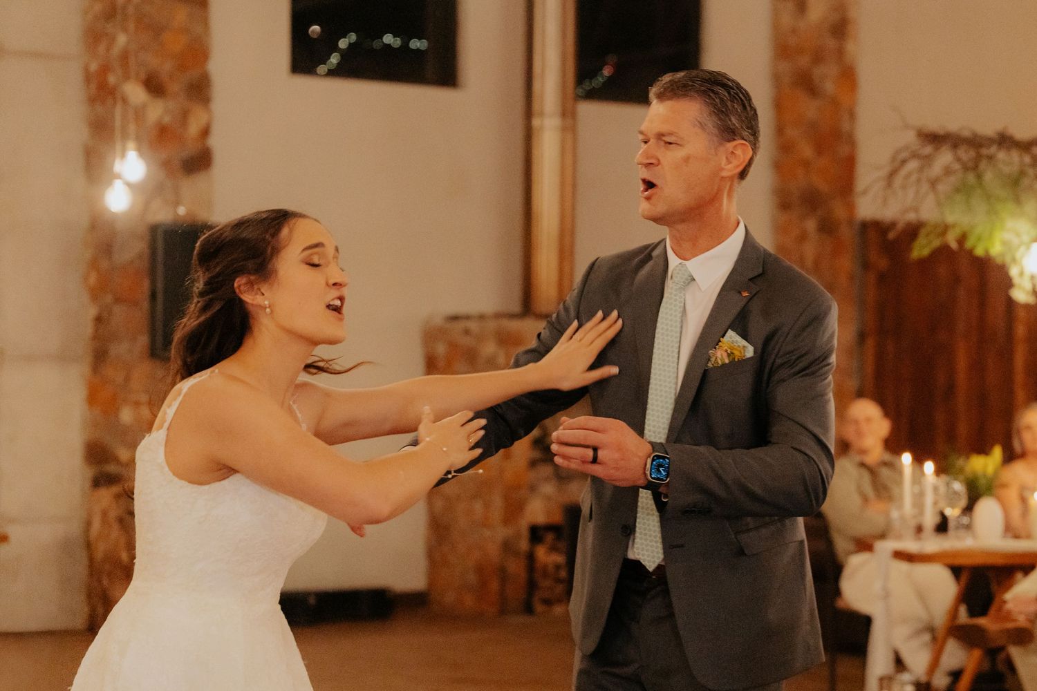 Newlyweds share playful moments on the dance floor during their first dance at an indoor reception venue.
