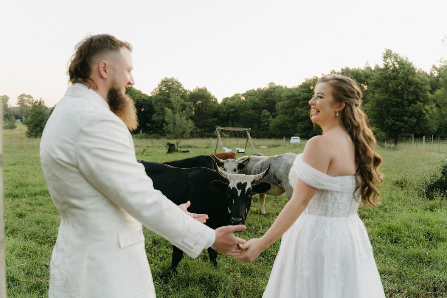 Couple in white wedding attire share romantic moment in sunlit meadow.