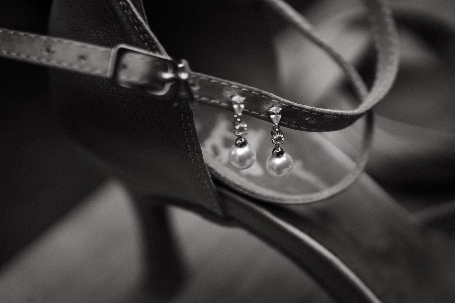 Close-up black and white photo of delicate earrings hanging on a ribbon.