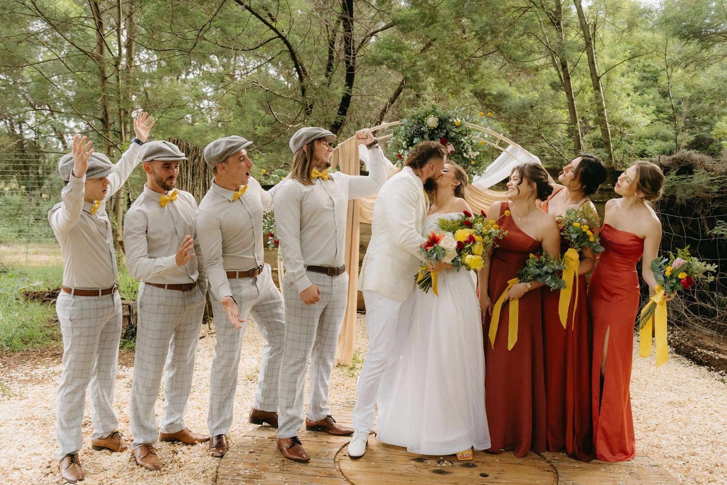 Wedding party poses outdoors with bridesmaids in burgundy dresses and groomsmen in light gray attire.