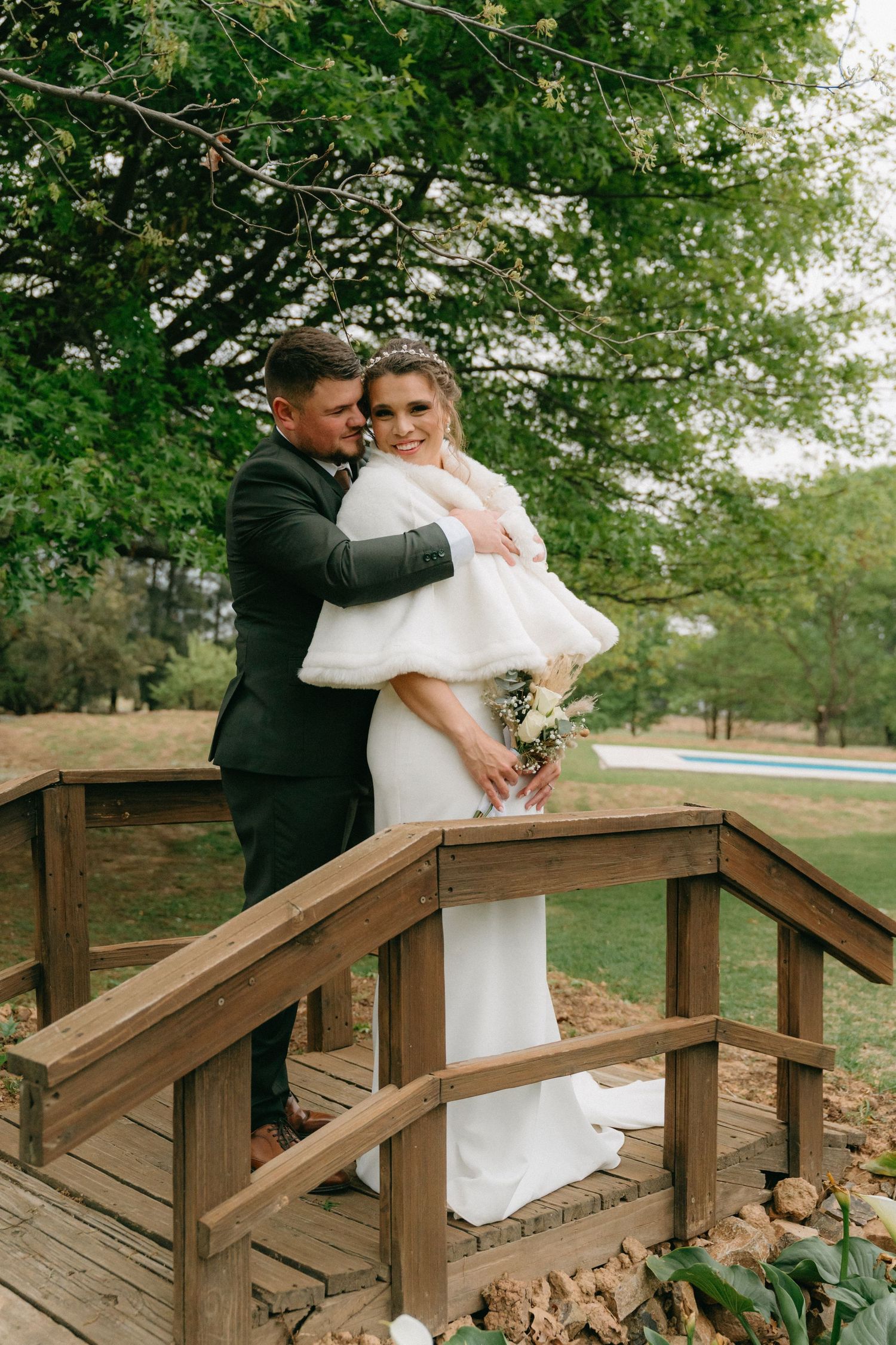 A couple shares an intimate moment on a wooden deck surrounded by lush greenery.