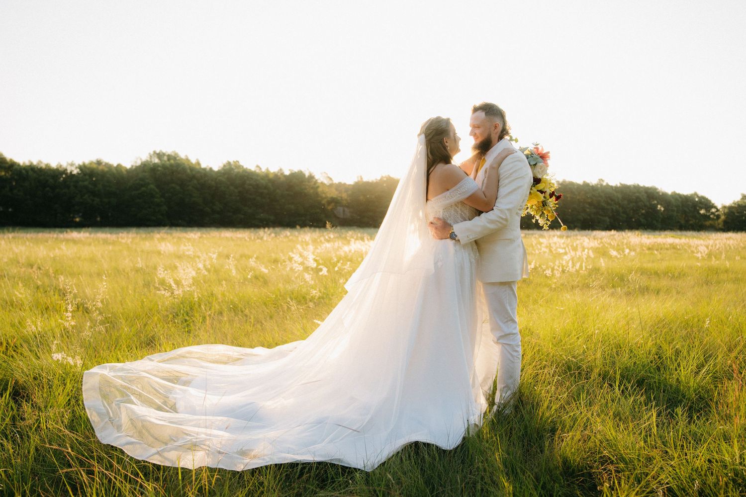 Bride and groom embrace in golden sunlit field, brides long veil flowing in the breeze in Pretoria, South Africa