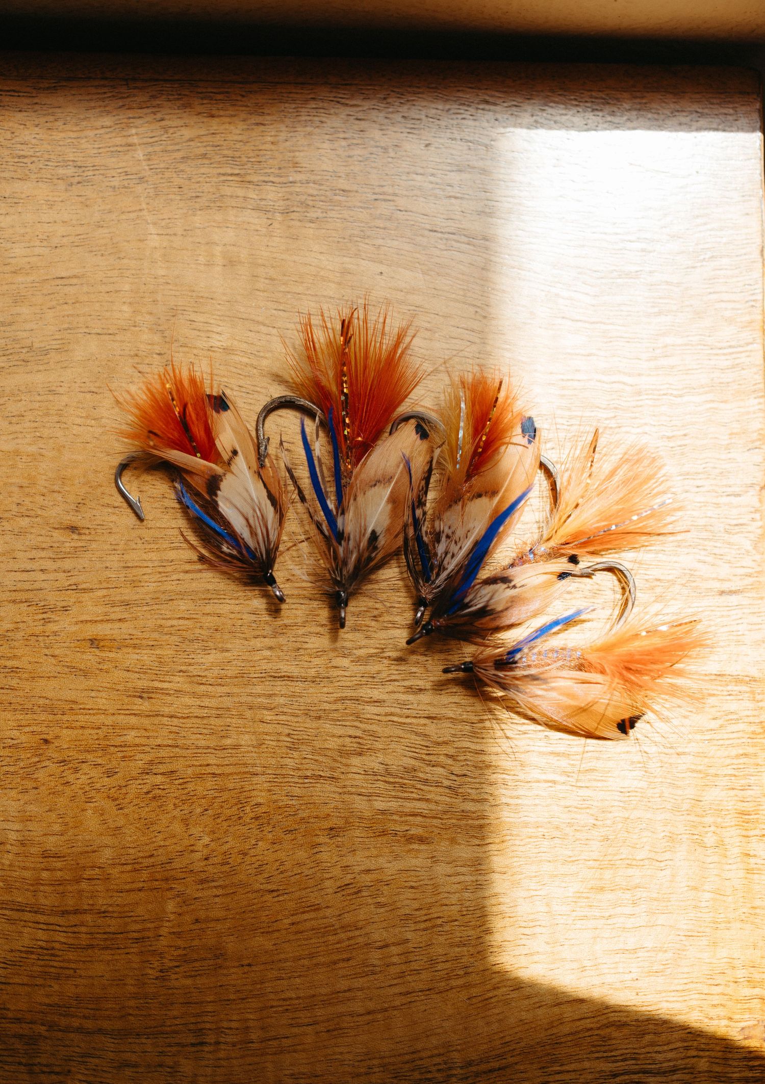 Artistically arranged orange and blue fishing flies on a wooden surface in natural lighting.