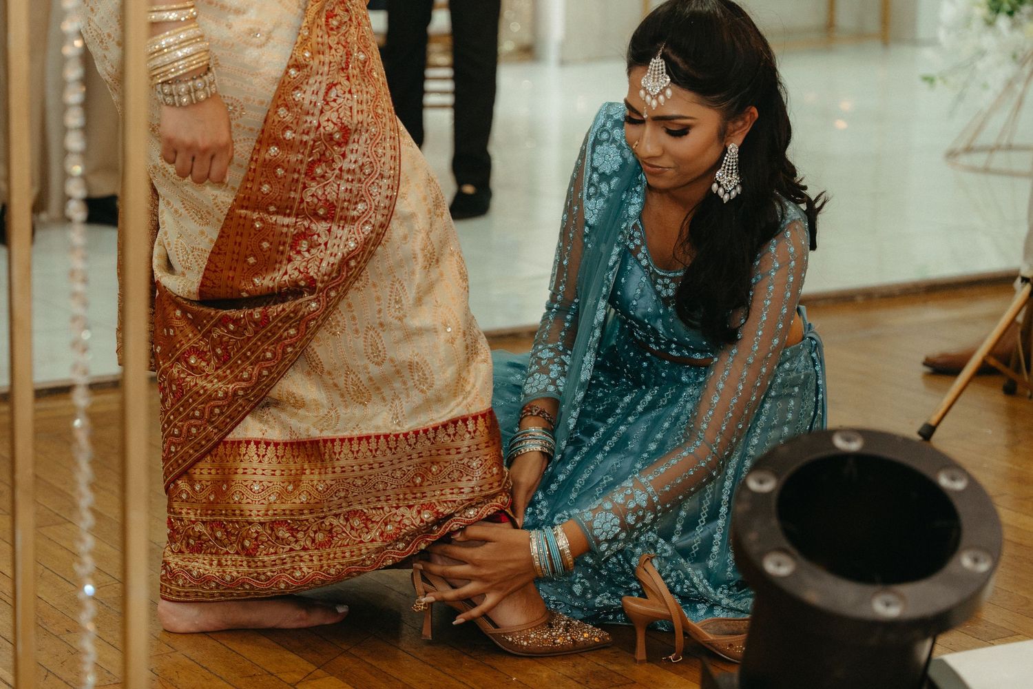 Bride in traditional South Asian wedding attire performs cultural ceremony with family members during celebration.