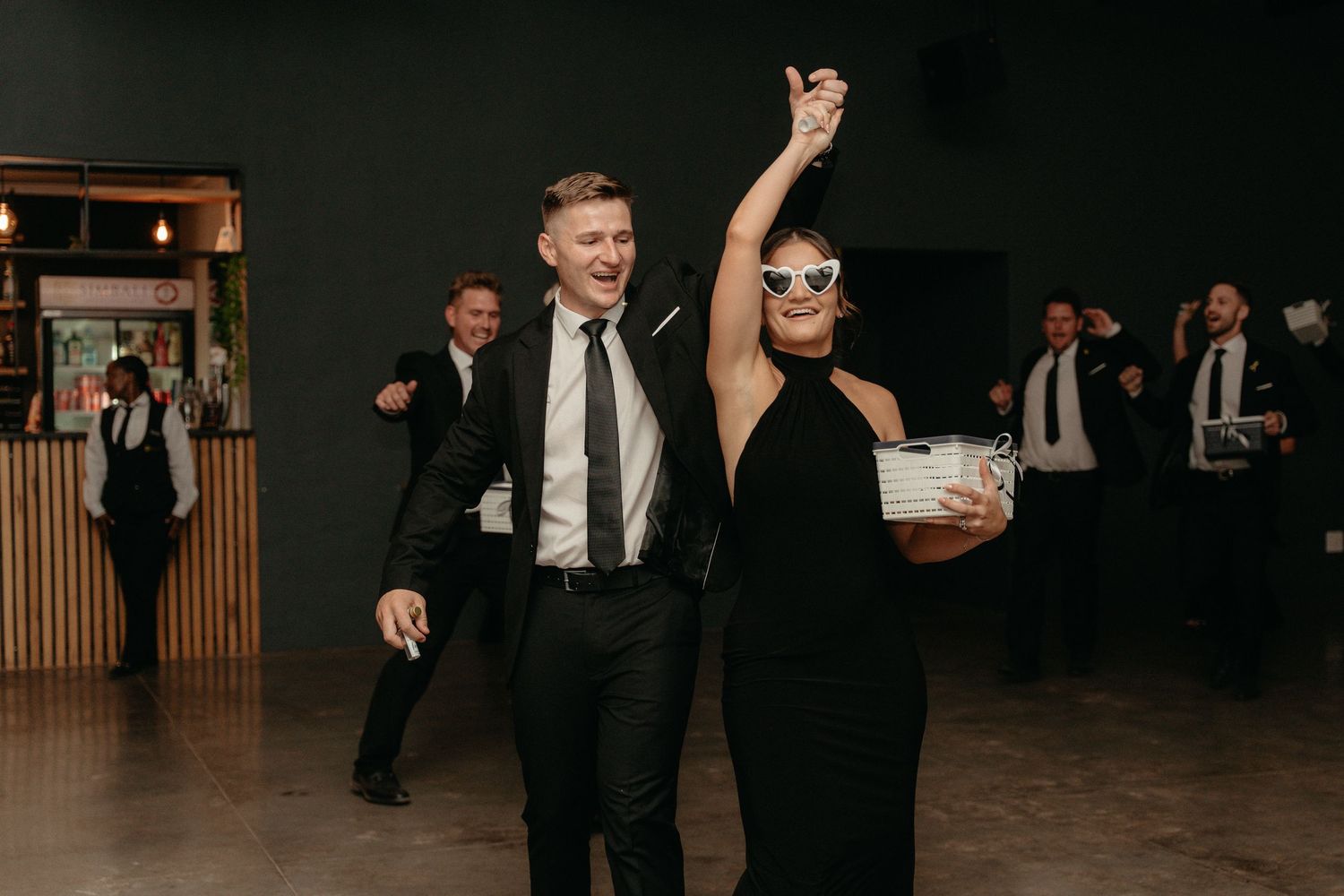 People in formal attire dancing and celebrating at an elegant wedding reception in a dark venue.