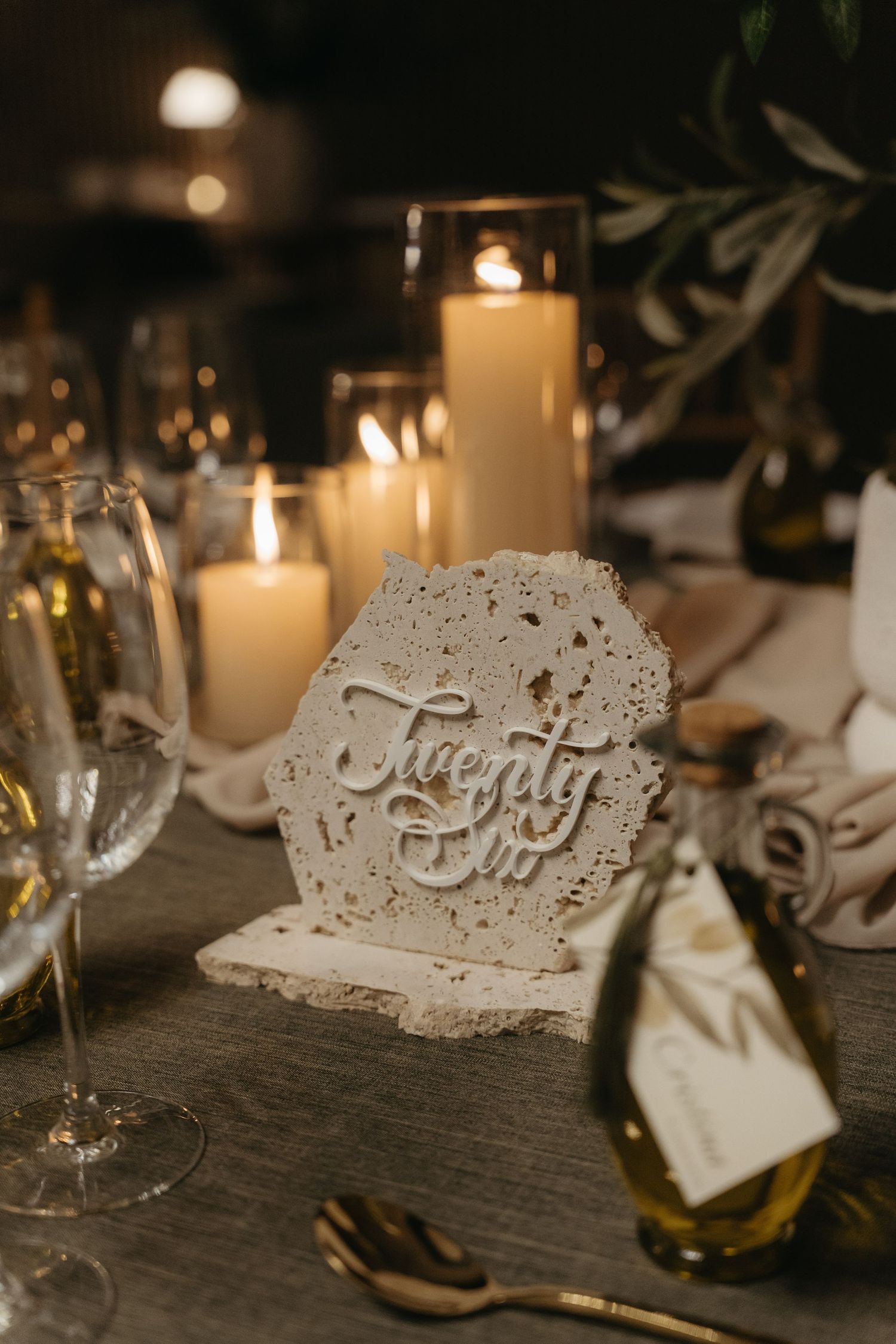Elegant wedding table setting with a travertine table number sign reading Twenty Six, glowing candles, and wine glasses.