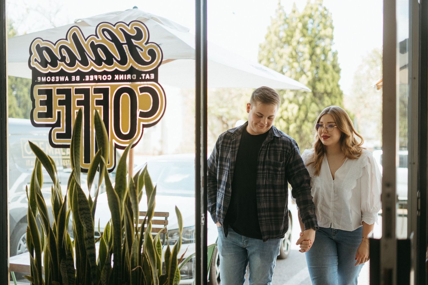 Through glass window showing lettering of coffee cafe with couple walking and laughing together inside.