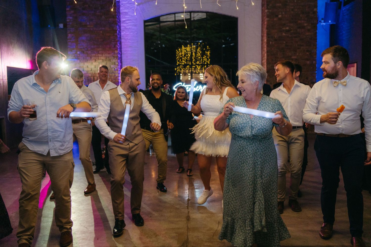 Wedding guests dance together on the reception dance floor under purple venue lighting and decorative elements.