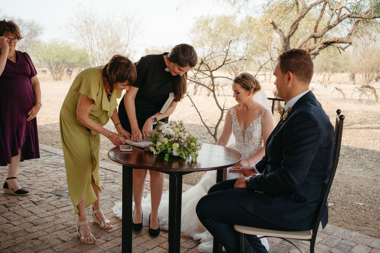 Wedding party members gather around a small table for document signing during ceremony.