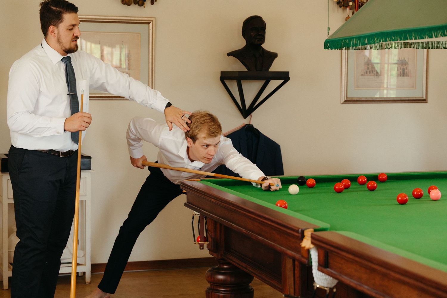 Players engage in a game of snooker on a green felt table in a well-lit indoor setting.