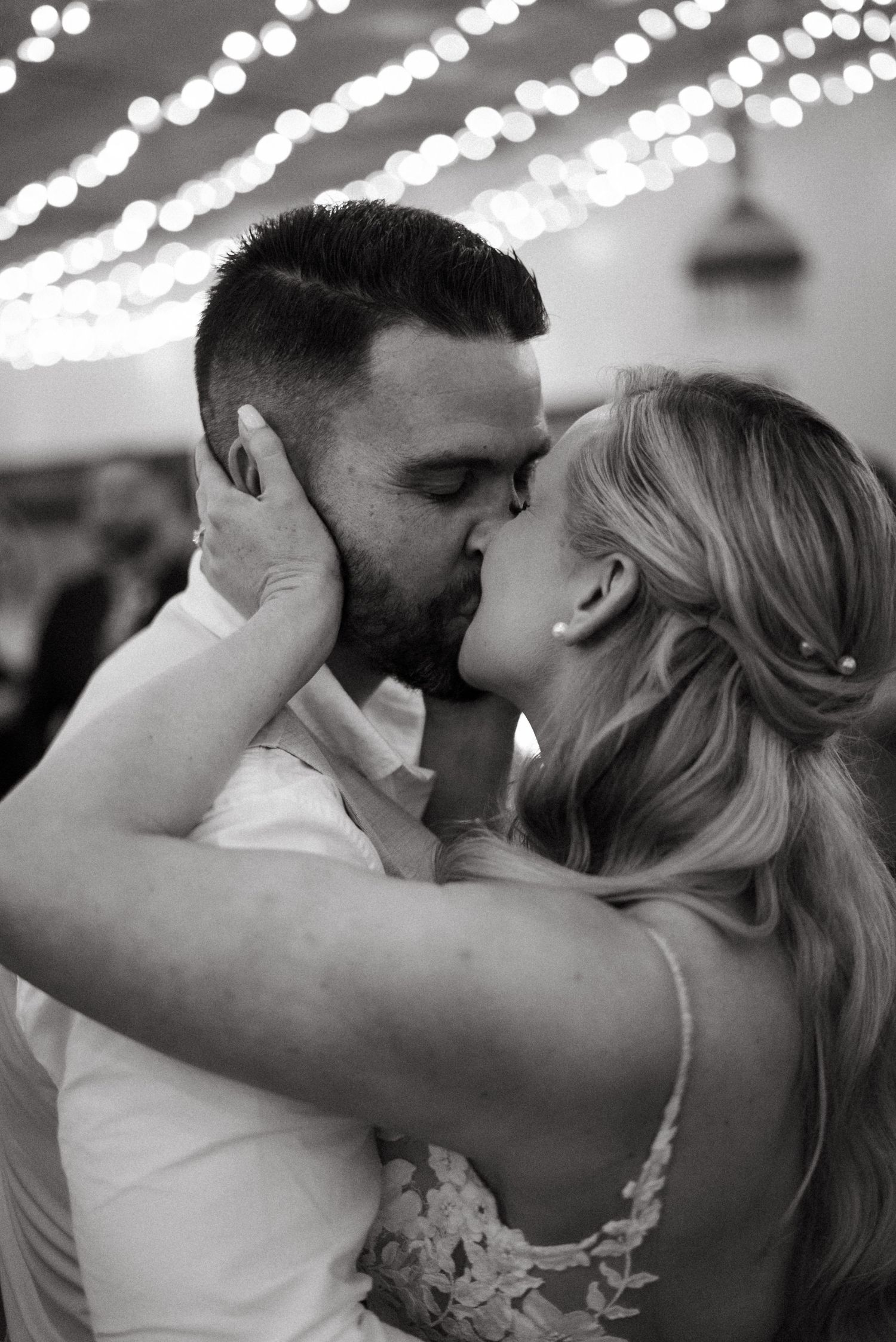 An intimate black and white photo of a couple sharing a romantic moment under string lights.