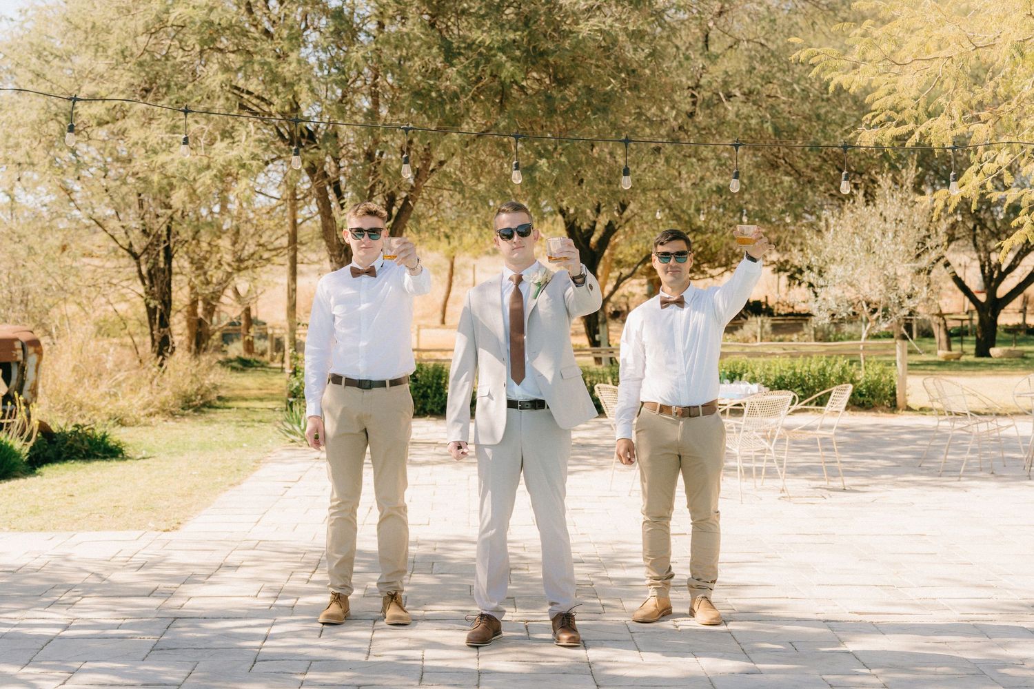 Wedding party in neutral tones stands together outdoors against a desert landscape backdrop.