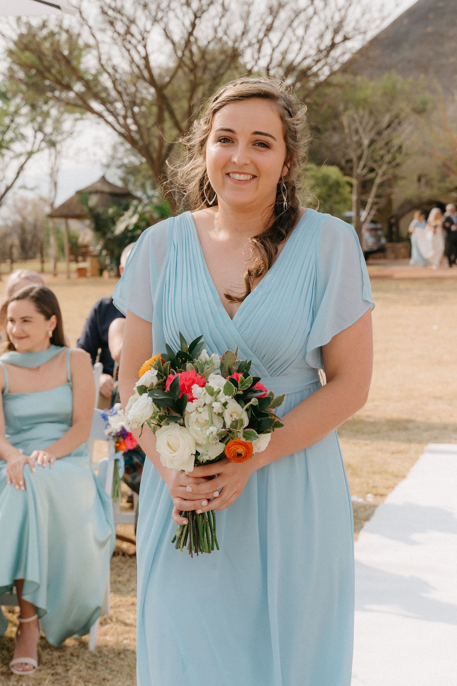 Bridesmaids in light blue dresses hold colorful bouquets during outdoor ceremony.