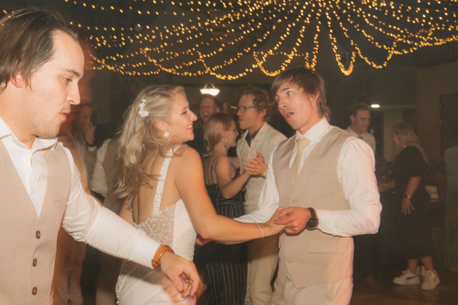 Couples dancing under twinkle lights at an indoor wedding reception.