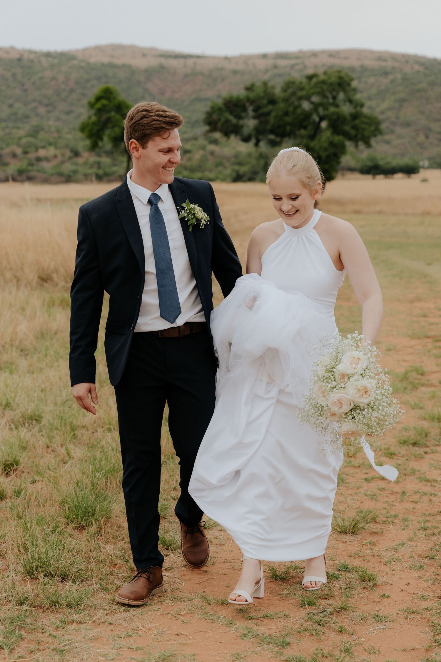A couple walks together through a scenic field with mountains in the background during their wedding.