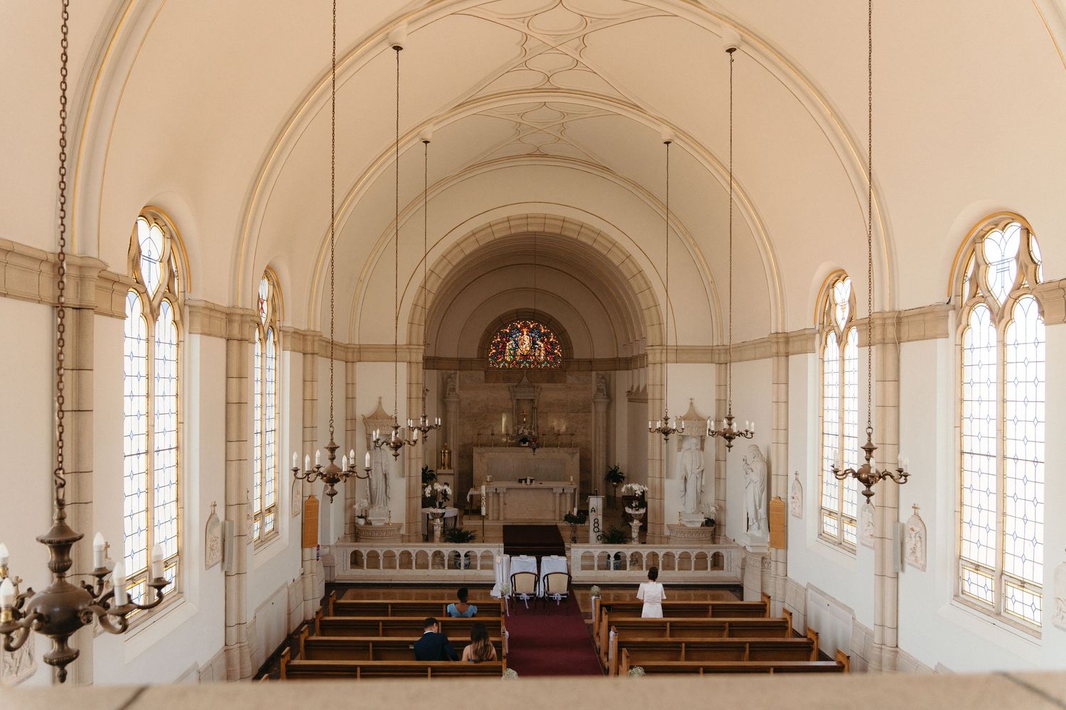 Interior view of a historic white church sanctuary with arched windows, wooden pews, and ornate chandeliers in Pretoria