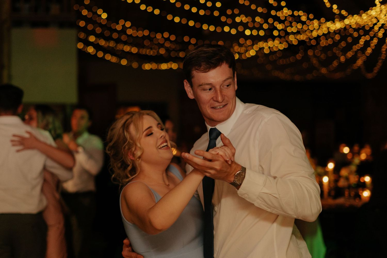 Wedding guests dancing beneath twinkling lights at an evening reception.