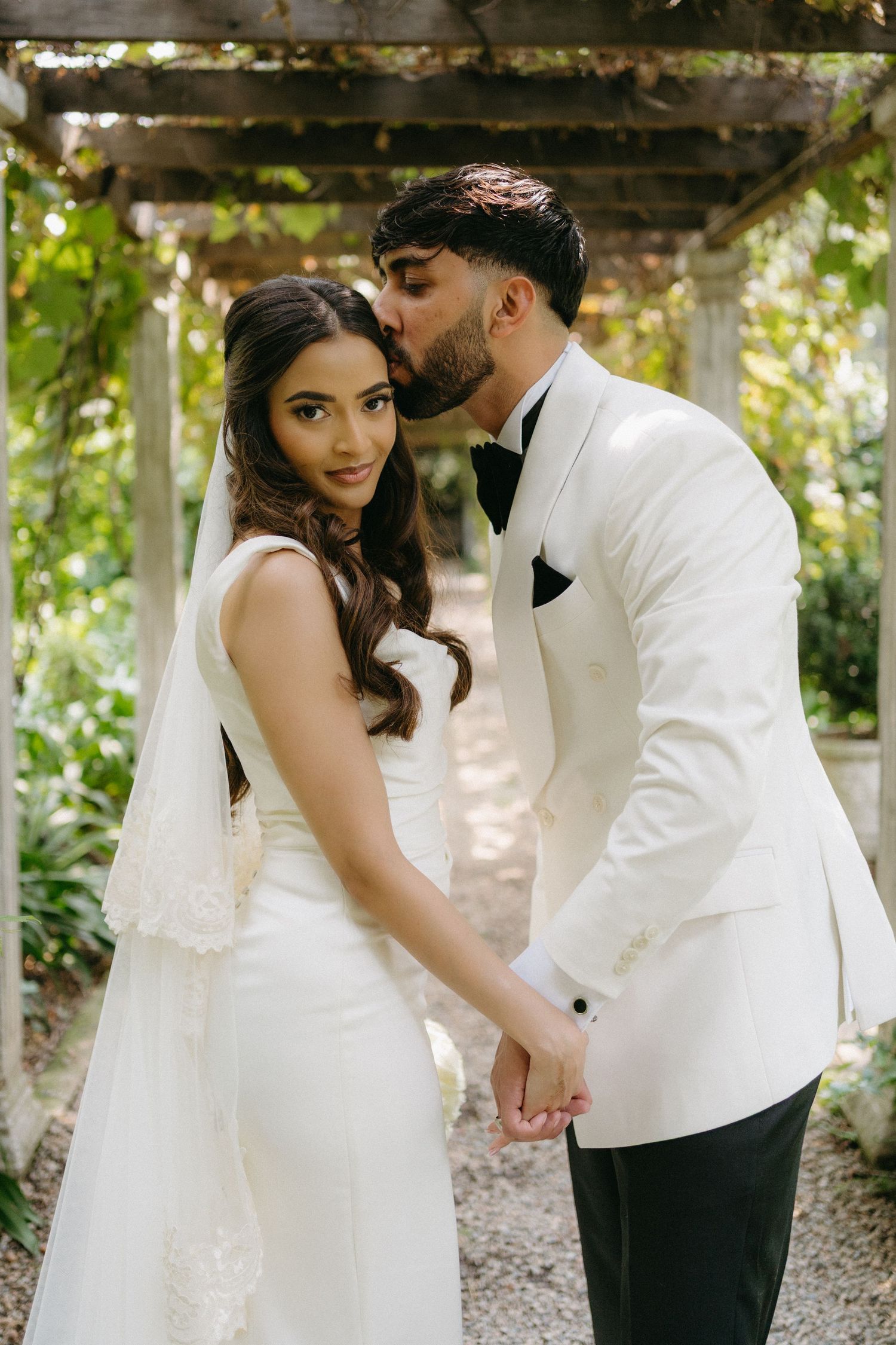 Intimate moment between newlyweds under a garden pergola covered in greenery.