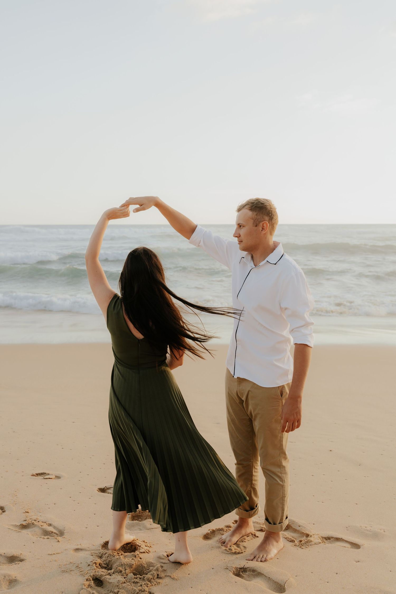A couple dancing together barefoot on a beach at sunset with the Mossel Bay ocean waves in the background.