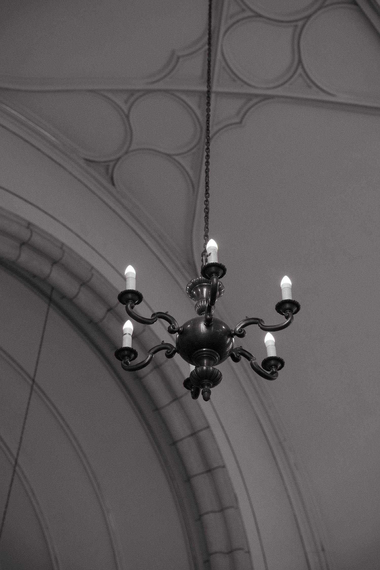 Black and white photo series showing a vintage chandelier in progressive stages of installation on an ornate ceiling.