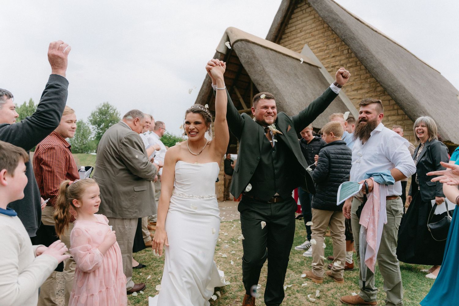 Wedding party and guests celebrate outdoors near a brick building.
