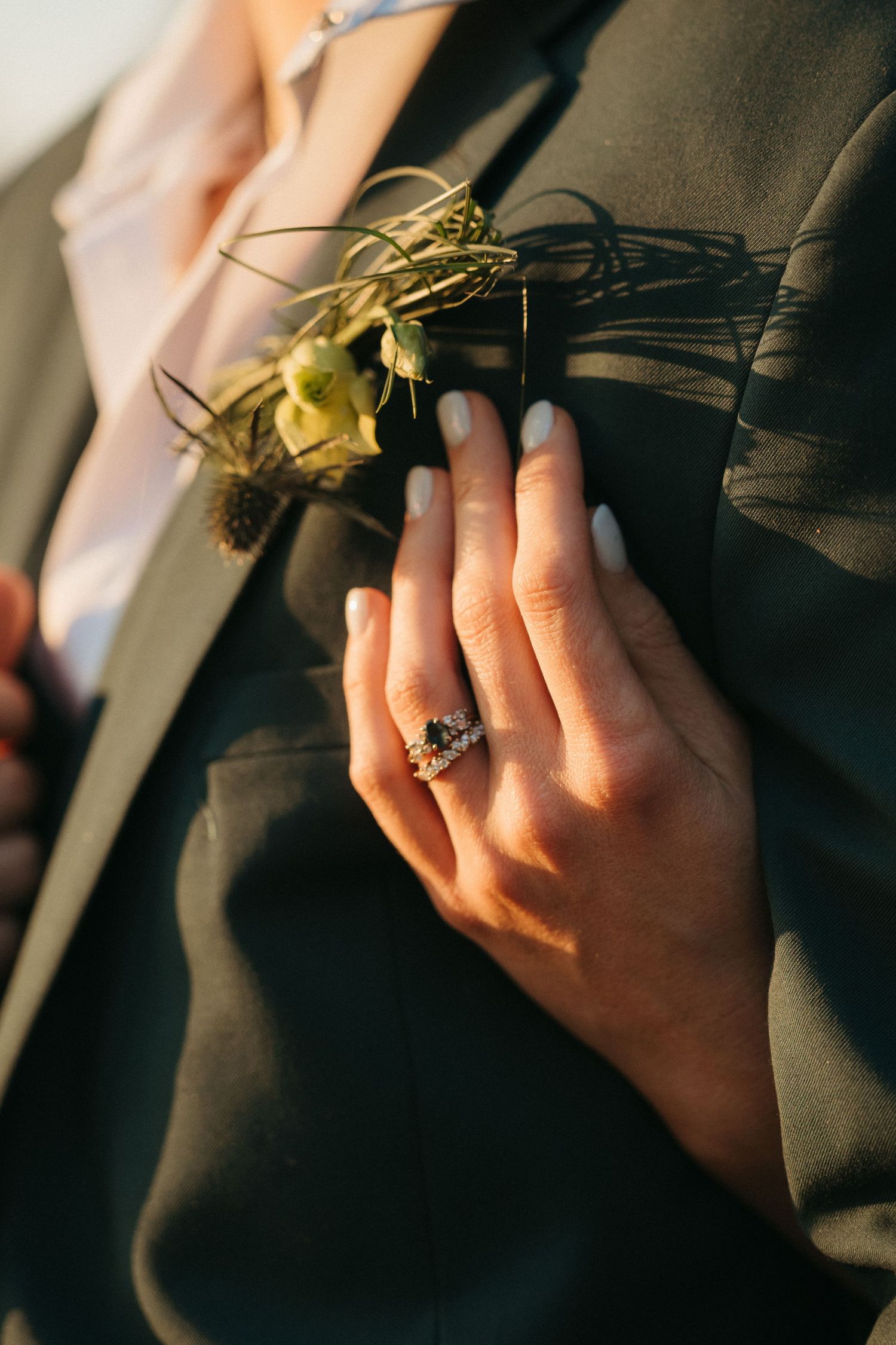 Close-up of a woman's hand wearing an elegant dark gemstone ring resting on a man's dark suit jacket with a boutonniere.