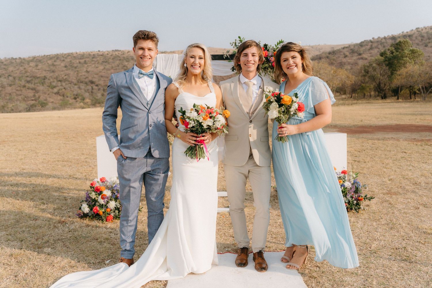 Wedding party poses together outdoors with bride in white dress and bridesmaids in blue.