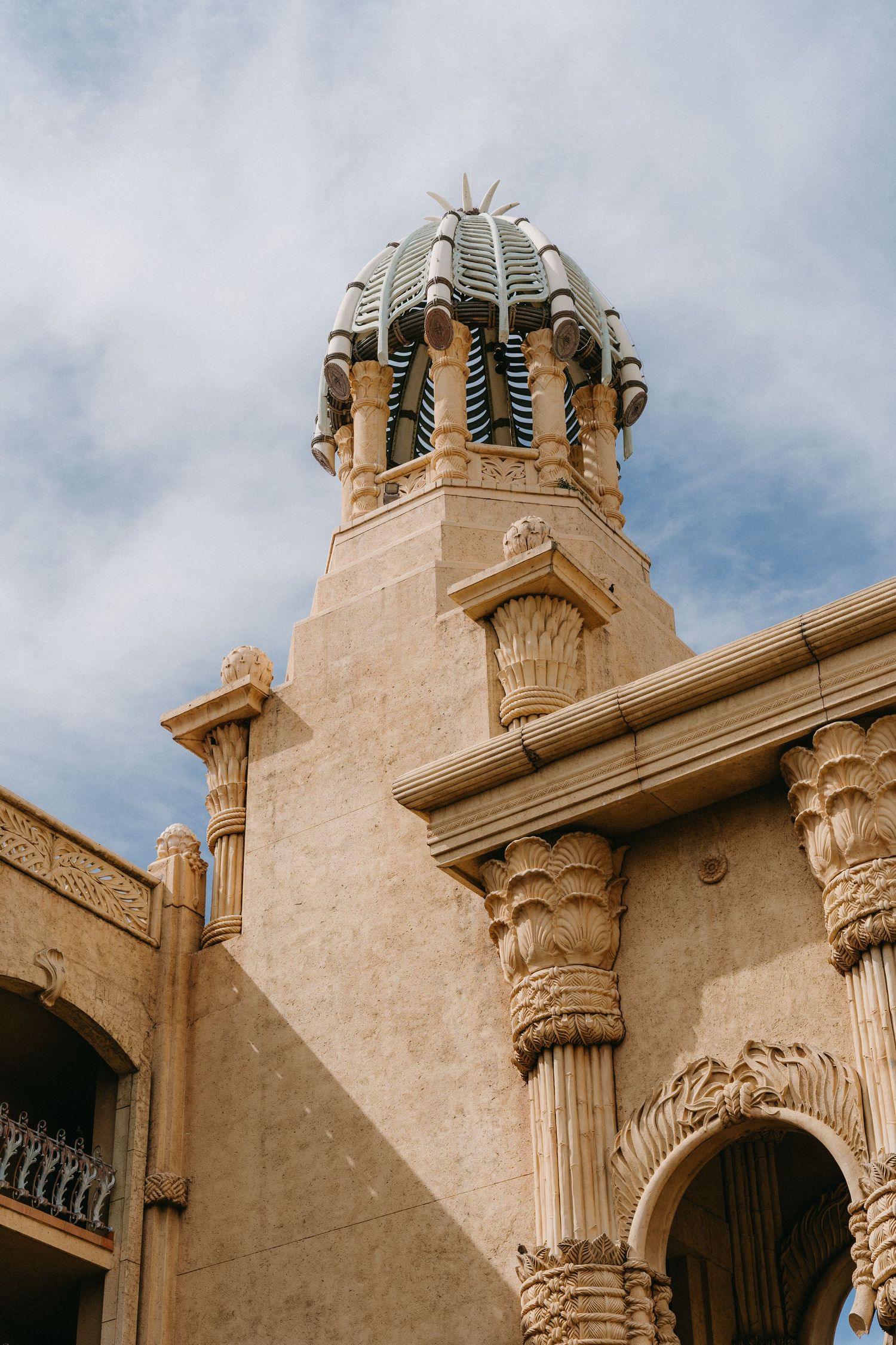 Architectural details of ornate stone columns and domed crown molding on a Mediterranean-style building against blue sky.