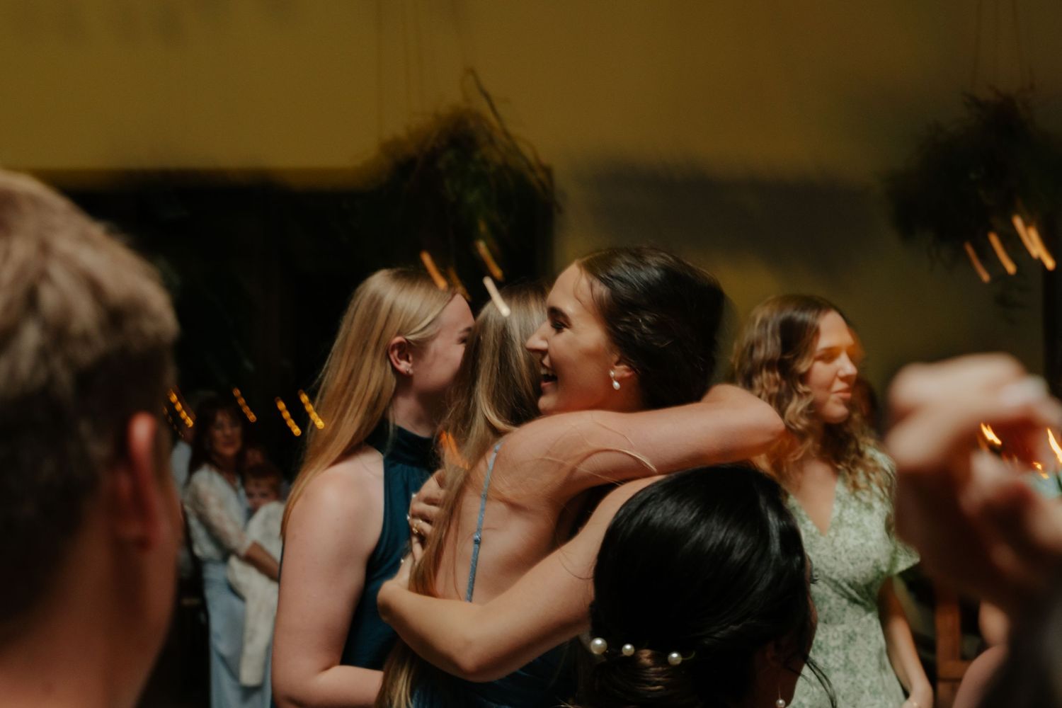 Wedding guests dance and embrace on a dimly lit dance floor during an evening reception celebration.