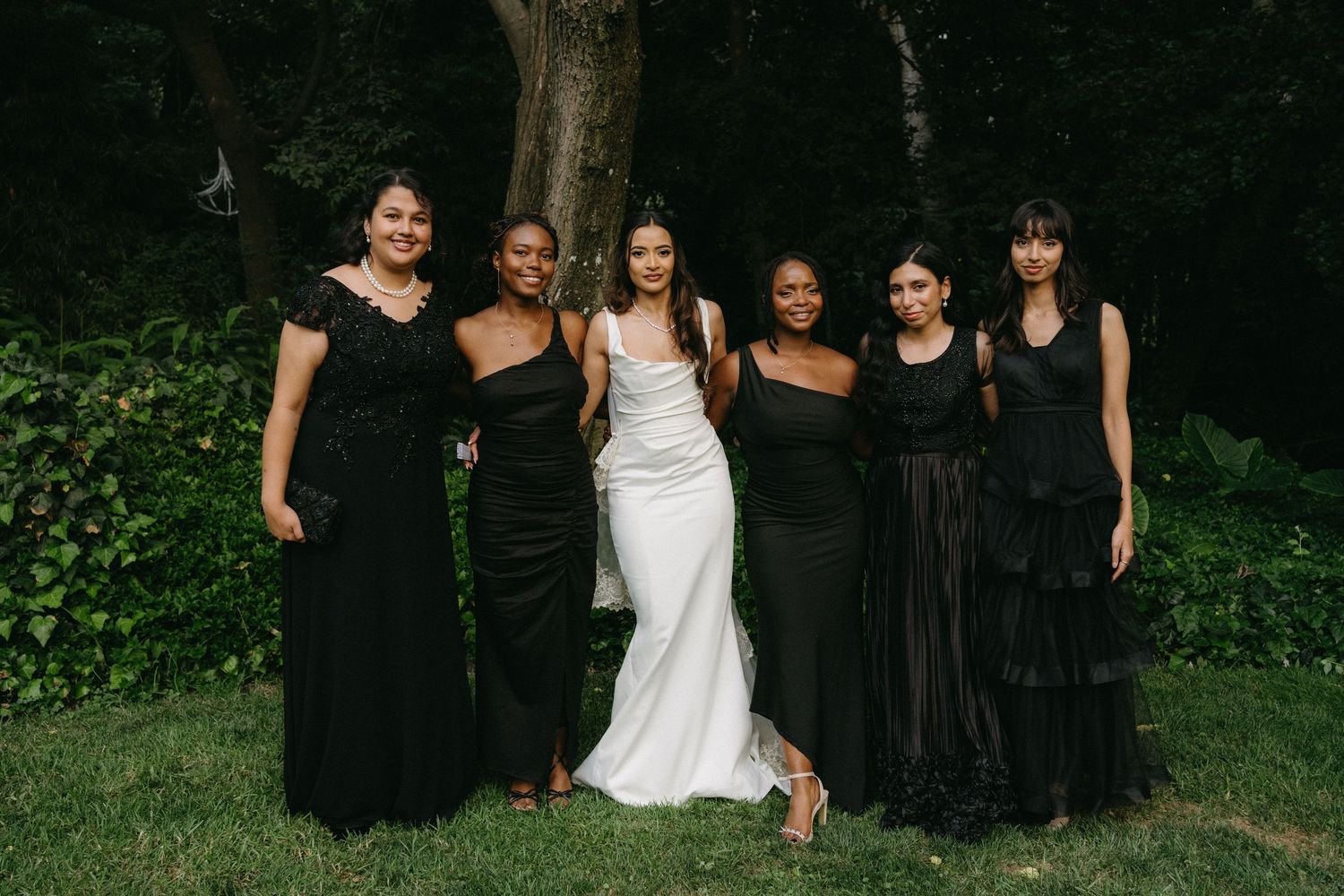 Wedding party photo with bride in white gown surrounded by bridesmaids in black dresses.