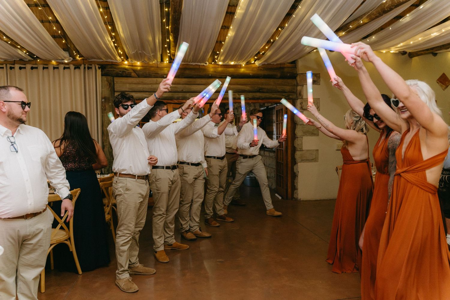 Wedding reception guests dancing and celebrating in a decorated indoor venue with string lights.