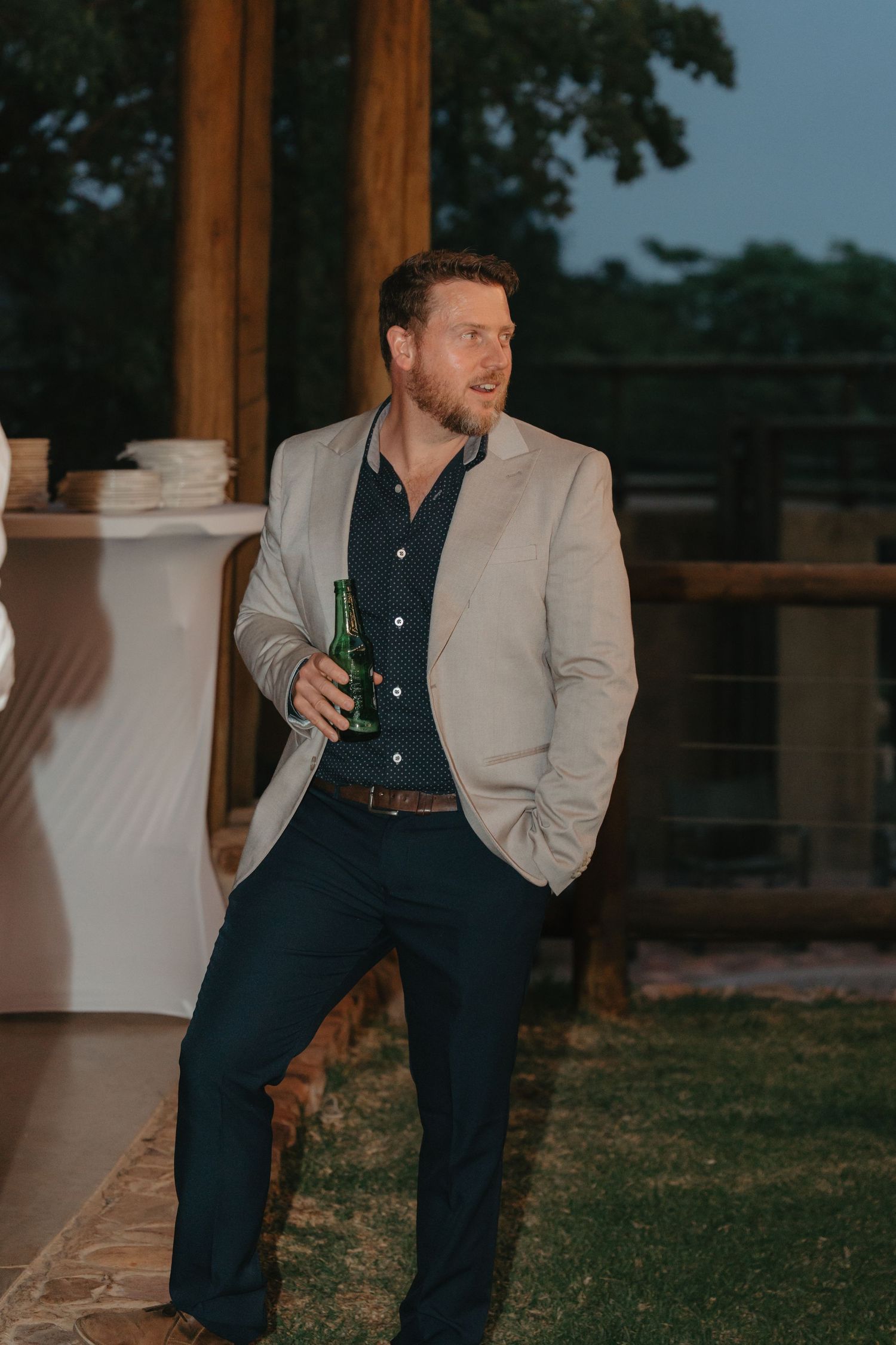 A person in a beige blazer and dark pants relaxes outdoors during golden hour.