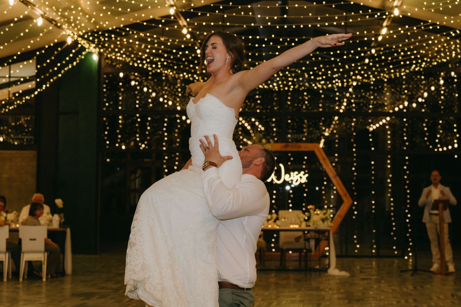 Couple dancing under twinkling lights during their wedding reception in a rustic venue.
