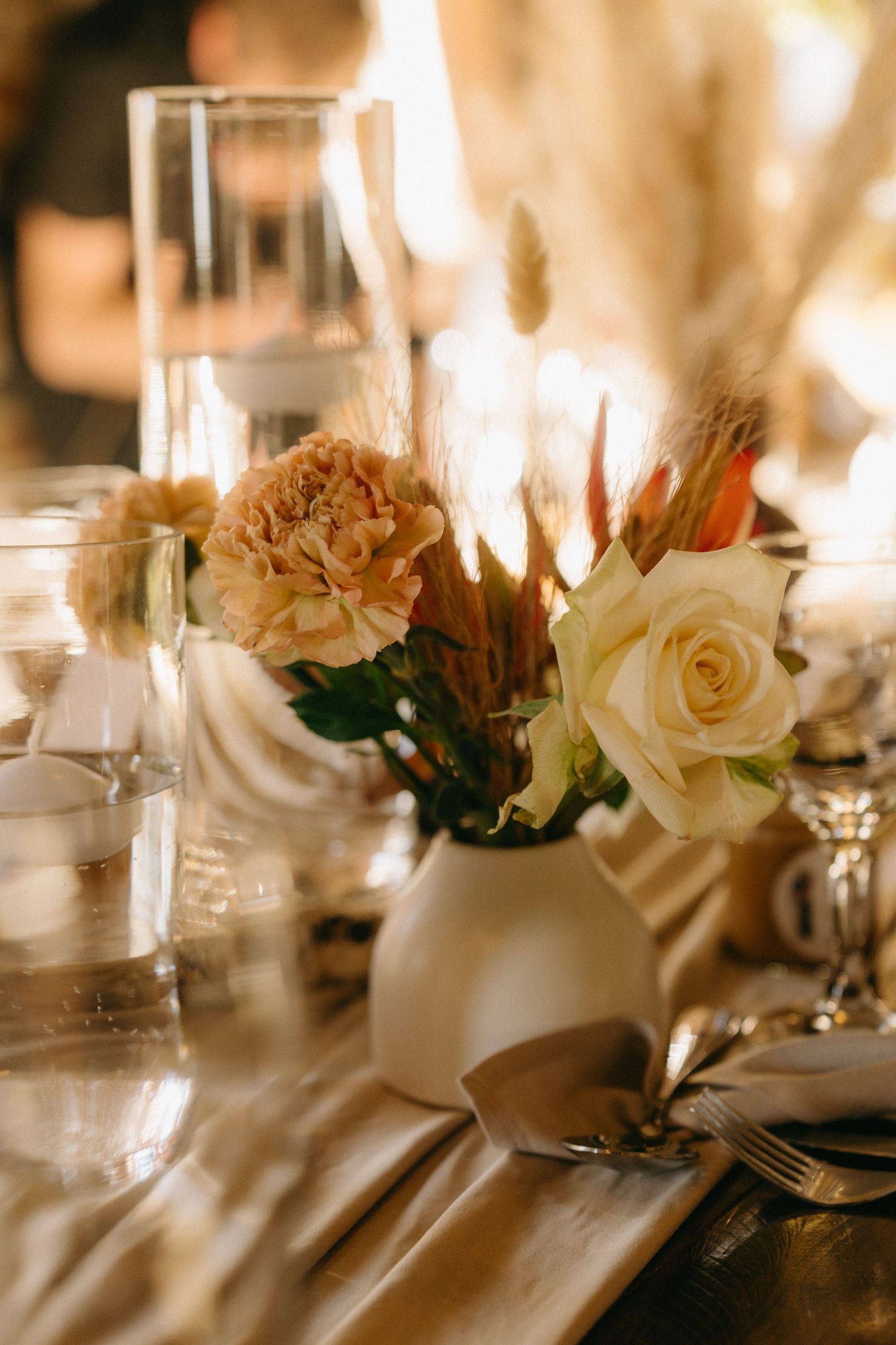 Elegant wedding table setting with white roses and candles in warm ambient lighting.