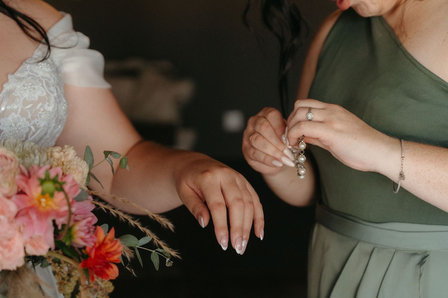 Hands shown putting on jewelry next to a pink and coral floral bouquet.