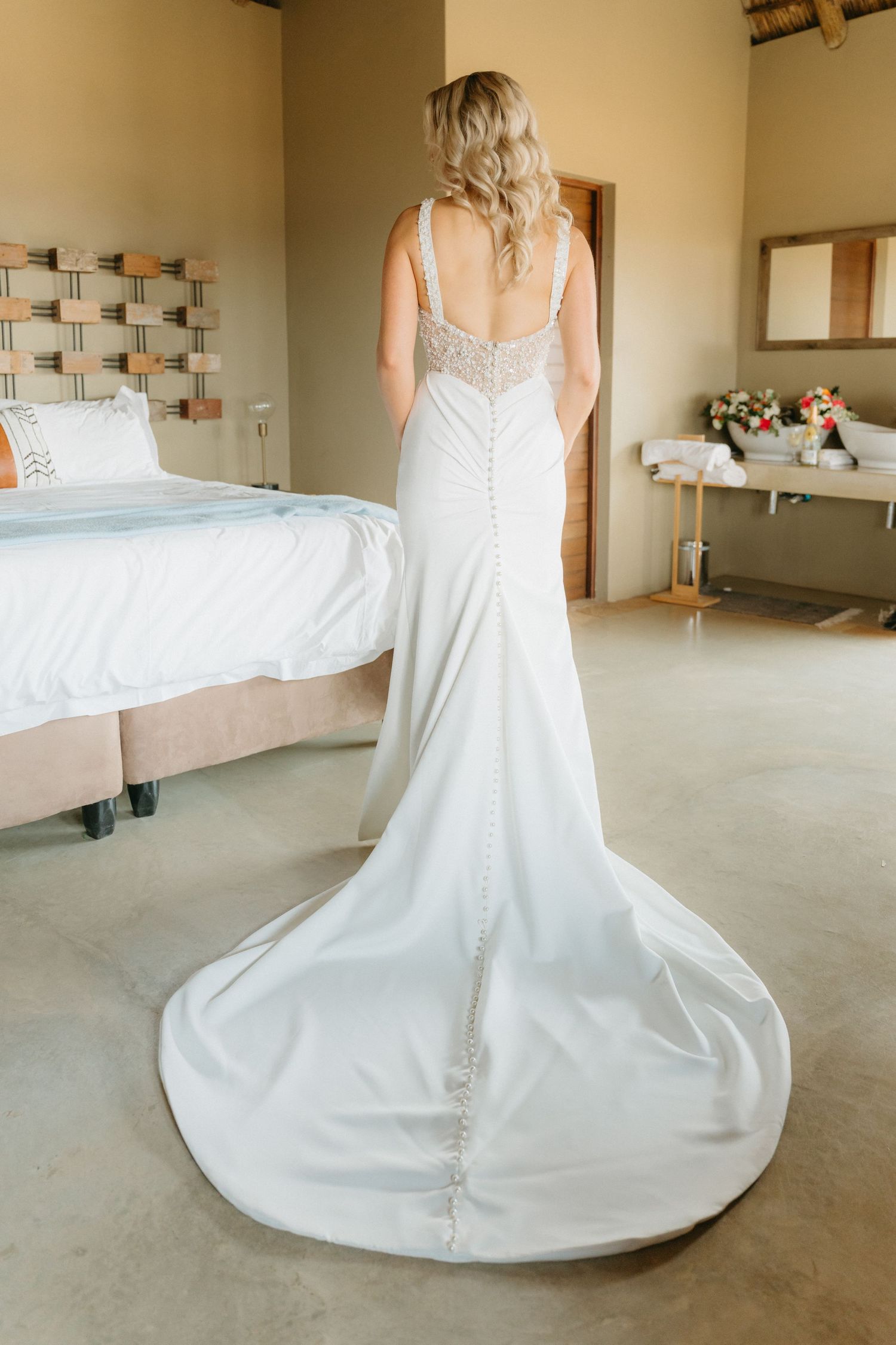 White wedding dress with flowing train displayed in a minimalist room setting.