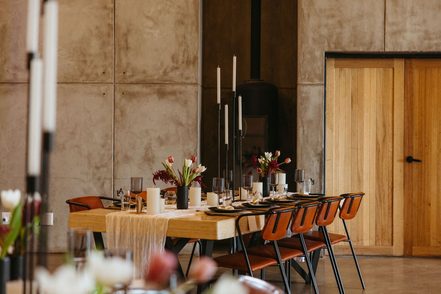 Long rustic dining table set for a wedding reception with wooden chairs and candle centerpieces.